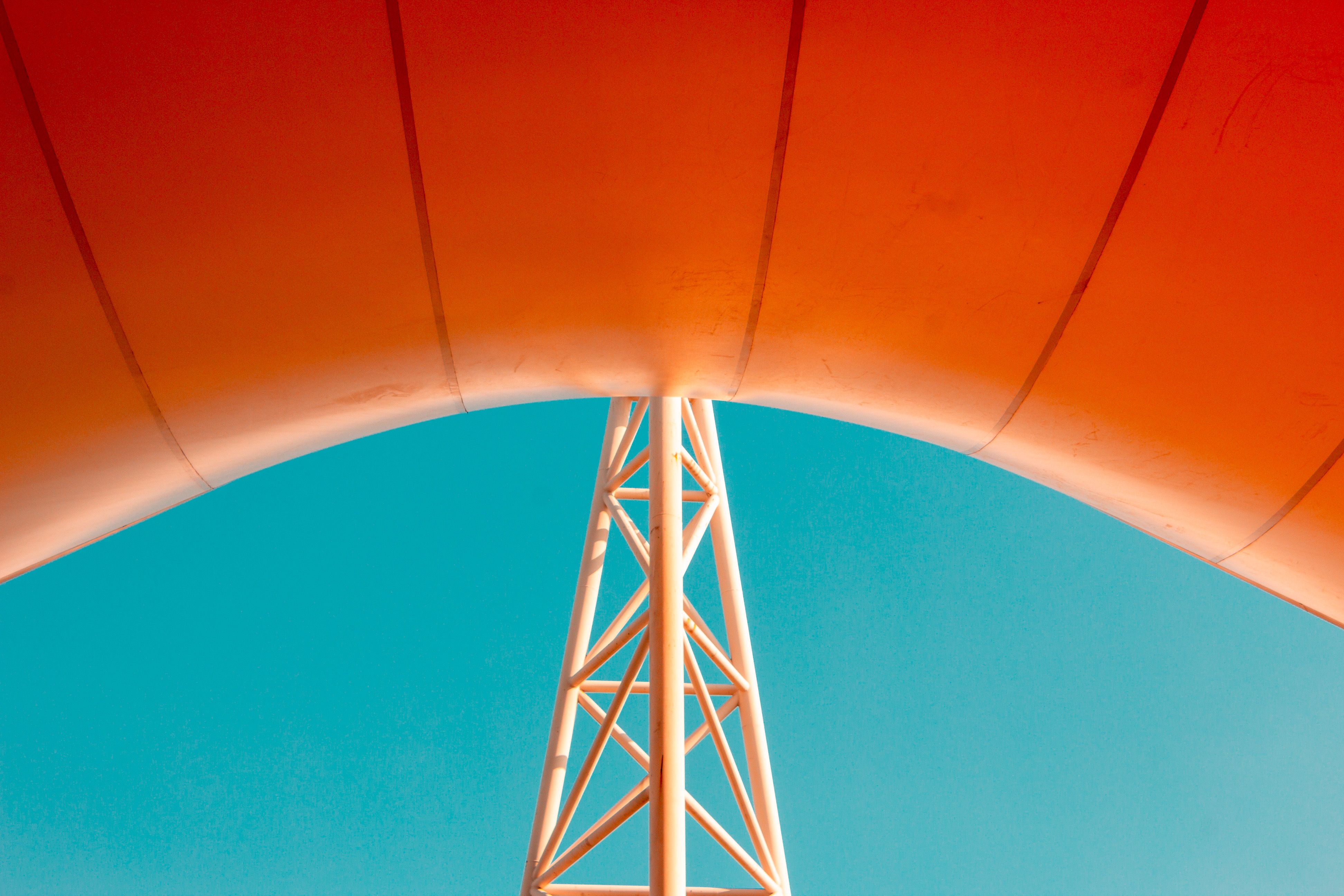 Orange canopy supported by a white steel truss against blue sky