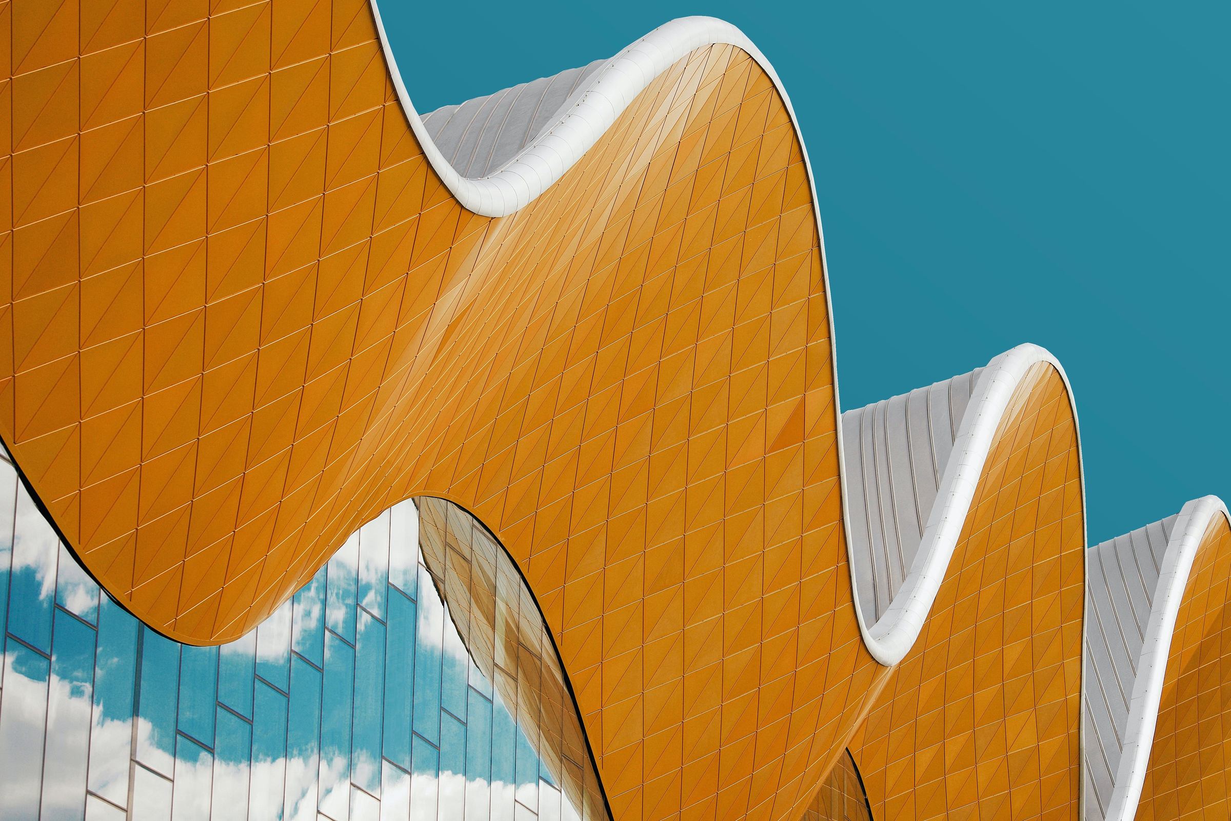 Undulating gold-tiled façade with white trim against a teal sky